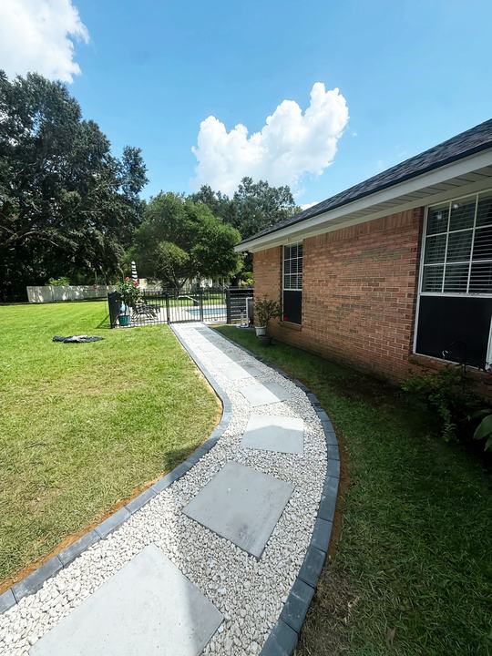 Curved walkway of stepping pavers and white gravel along a brick home