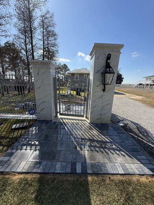 Gray paver landing in front of a metal walk gate between two white columns with a black lantern
