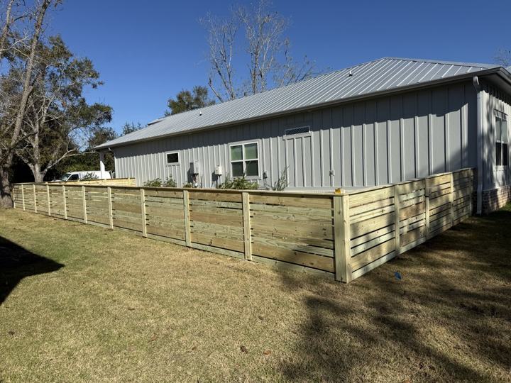 Modern horizontal-board wood fence enclosing the yard of a gray metal-roof home
