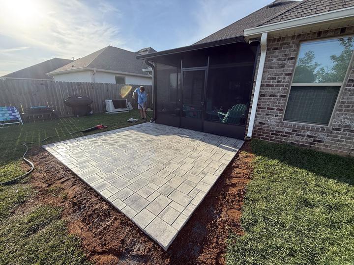 Gray paver patio extending from a screened porch on a brick home