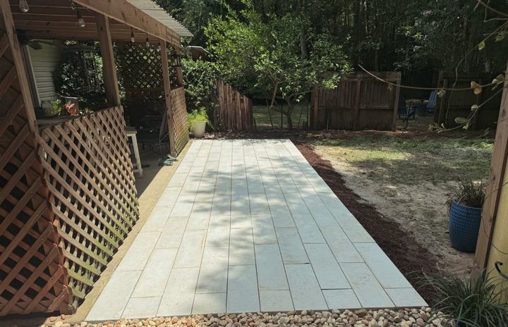 Long light-gray large-format paver patio extending from a covered lattice porch into the backyard