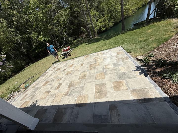Large multi-tone paver patio in a green backyard overlooking a waterway