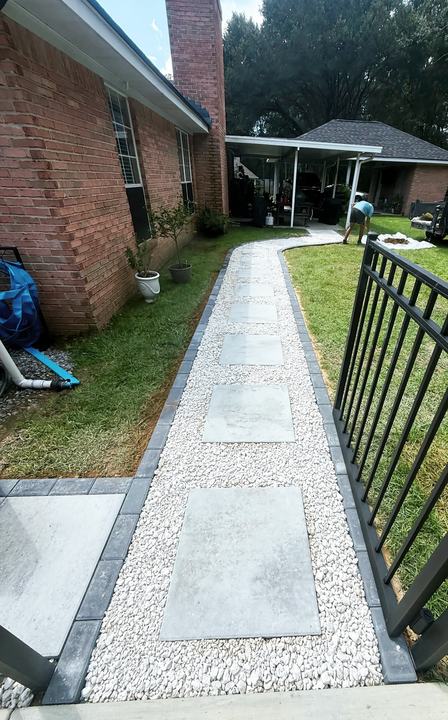 Walkway of large gray stepping pavers set in white gravel with a dark paver border beside a brick home