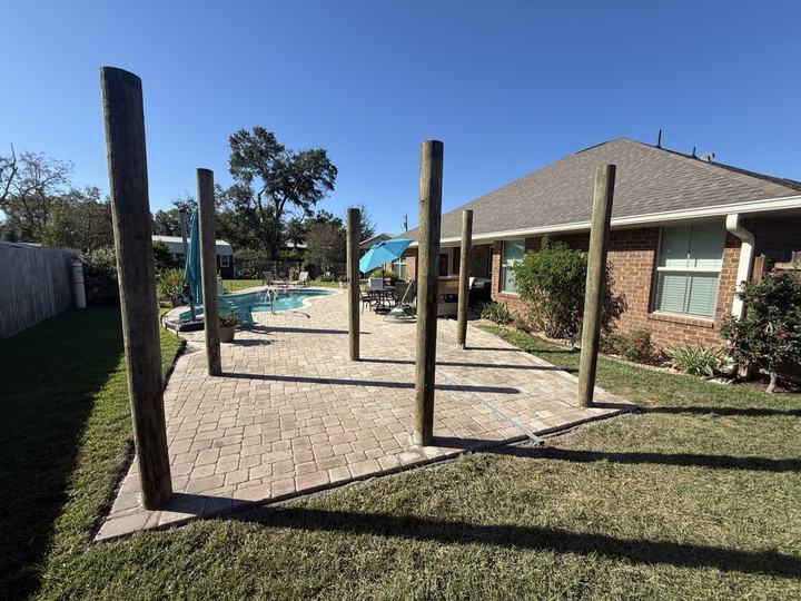 Brick paver patio with tall wood posts beside a backyard swimming pool