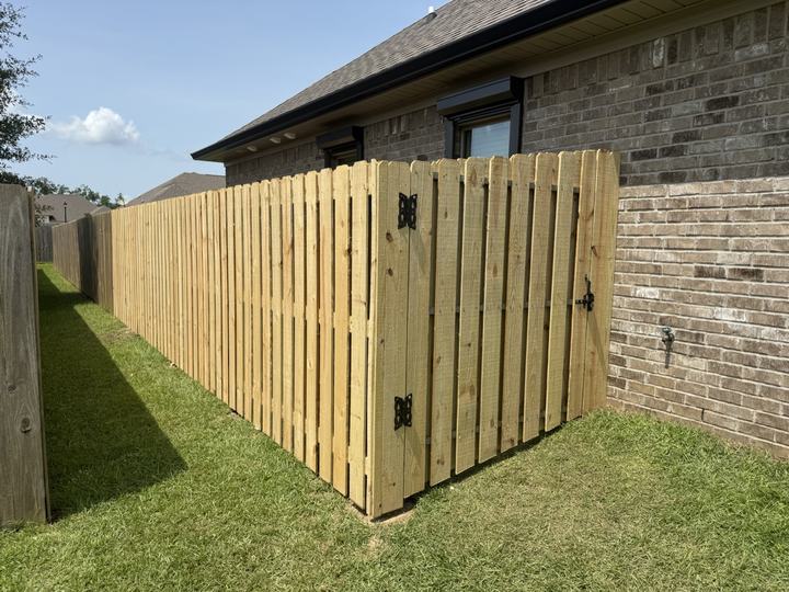 Shadowbox wood fence with a walk gate beside a brick home
