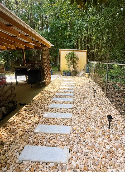 Path of stepping stones set in tan river gravel leading to a backyard shed