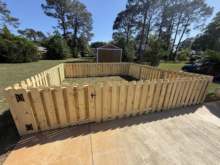Square wood fence enclosure with a walk gate and black hinges beside a driveway