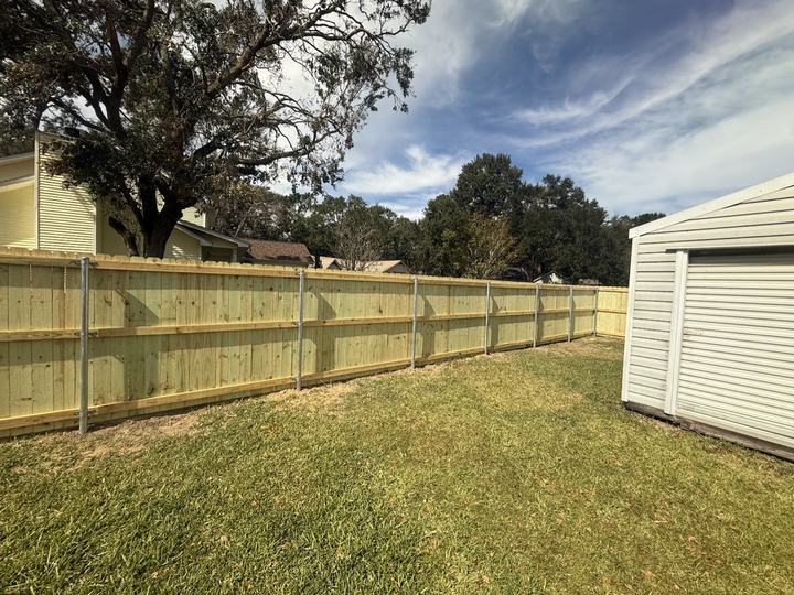 New wood privacy fence running along a grassy backyard beside a shed
