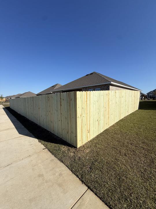 Long wood privacy fence wrapping the corner lot of a brick home under a clear blue sky